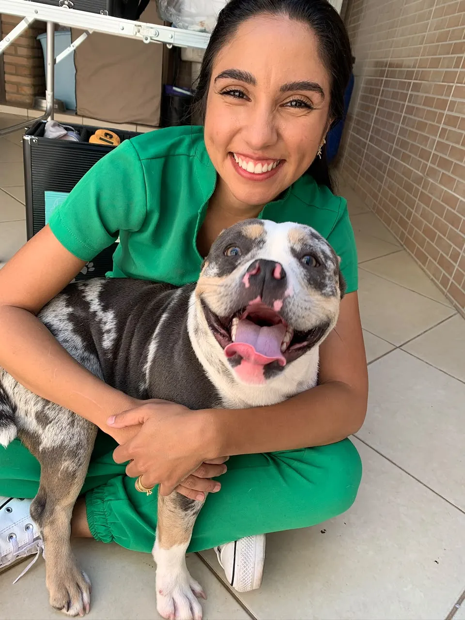 Dra. Natália abraçando um bulldog sorridente durante atendimento em casa